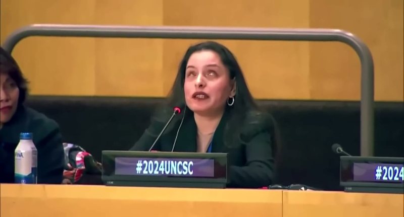 Priscilla Garces speaking into a microphone at a conference desk marked #2024UNCSC.